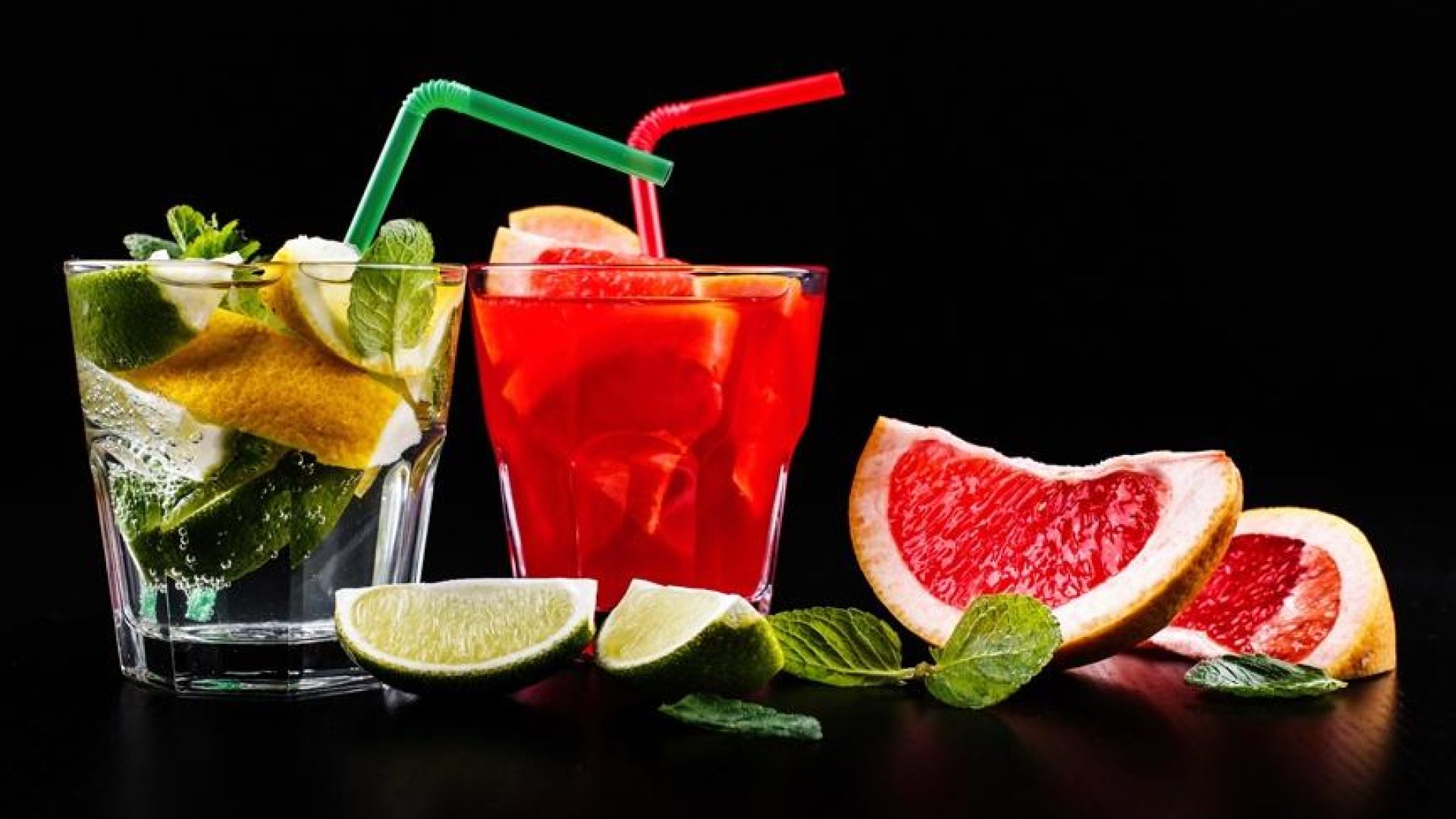 Delicious mojito, rum and cola, blood orange and vodka cocktails served with fruit, mint and ice stand on black table  table